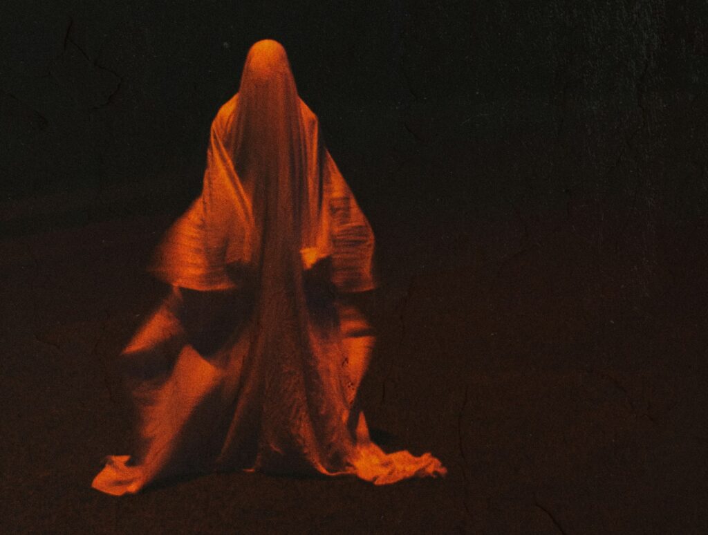 Ein verschwommenes Foto zeigt eine orange leuchtende Gestalt in weiten Gewändern im Dunklen